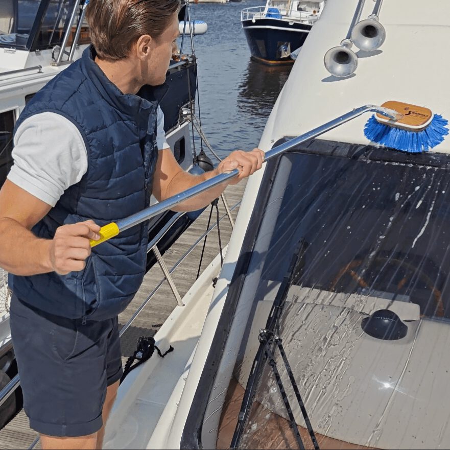 Medewerker houdt een schoonmaakborstel vast en maakt oppervlak boven het raam van een boot schoon