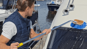 Medewerker houdt een schoonmaakborstel vast en maakt oppervlak boven het raam van een boot schoon