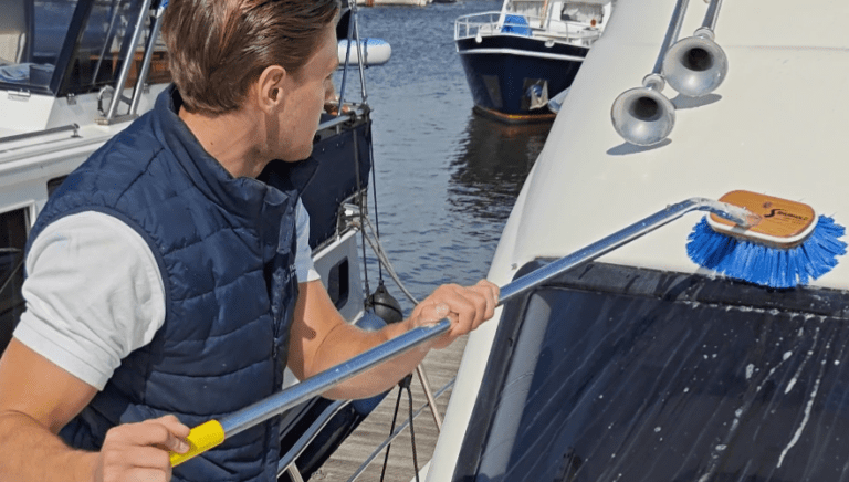 Medewerker houdt een schoonmaakborstel vast en maakt oppervlak boven het raam van een boot schoon